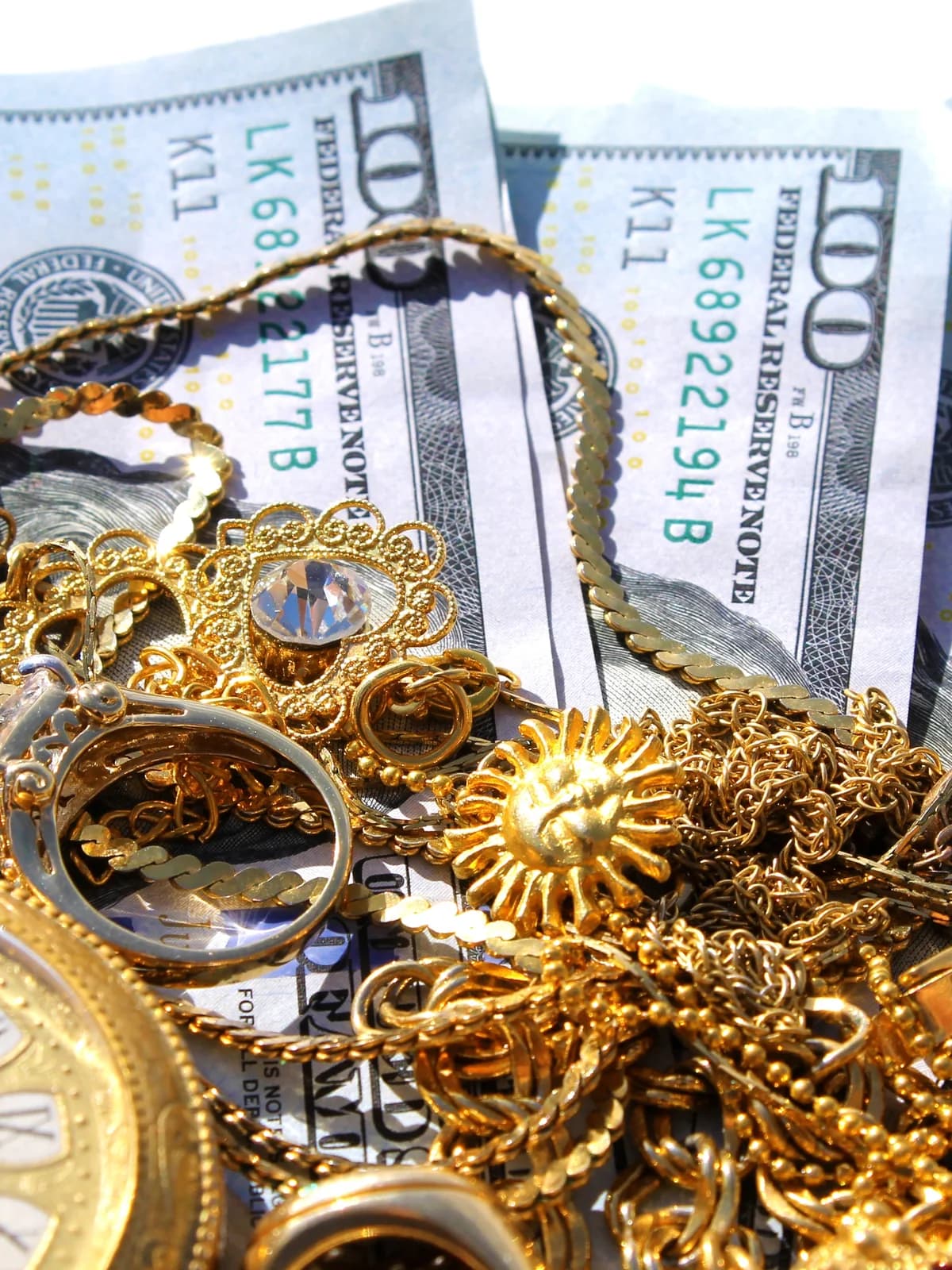 Gold chains, rings, and a pocket watch laid over hundred-dollar bills